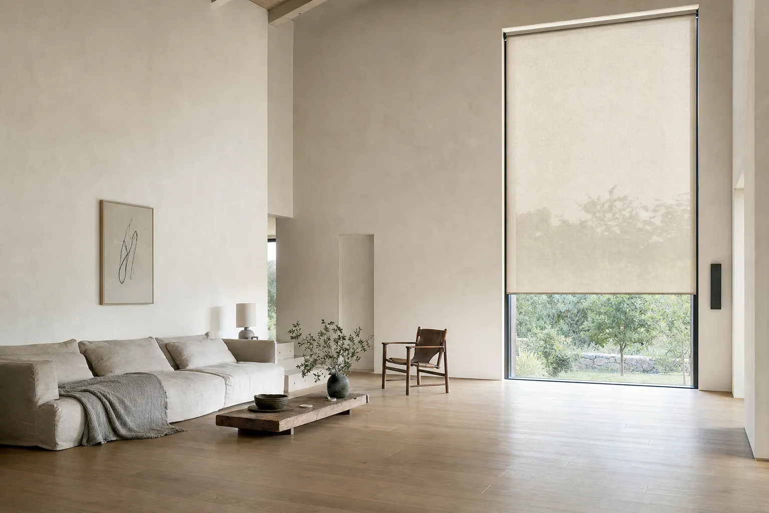 A wide, bright room with a tall window on the right carrying a single roller blind — one flat continuous plane of screen fabric with the garden faintly visible through the weave, and clear glass below it