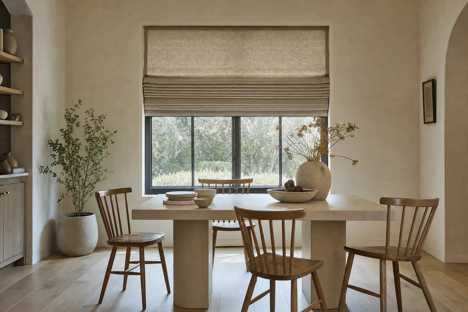 A roman shade raised halfway in a bright dining room, its linen gathered into soft horizontal folds stacked above the glass
