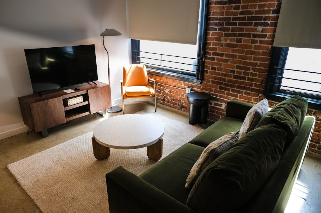 Living room with a television facing tall windows fitted with roller blinds